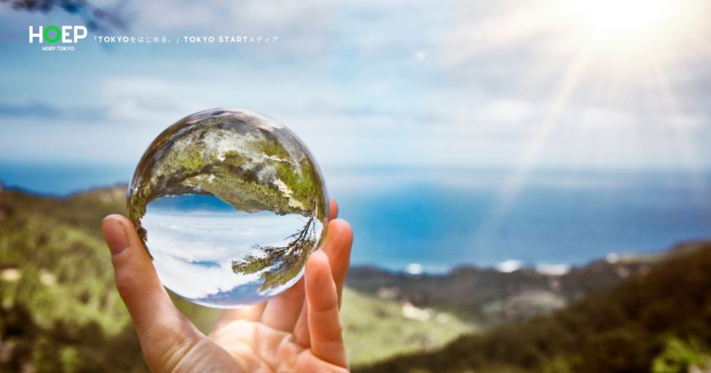 手のひらに乗せたクリスタルボール越しに海や山が見える画像
