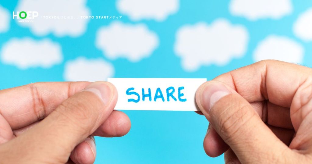 青空と雲を背景に「SHARE」と書かれた紙を持つ手の写真